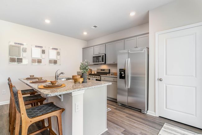 Kitchen featuring appliances with stainless steel finishes, gray cabinets, a kitchen bar, wood finished floors, and light stone countertops | Image 6