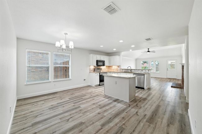 Kitchen featuring stainless steel appliances, a chandelier, light wood finished floors, open floor plan, and a center island | Image 5