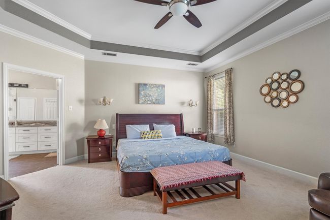 Bedroom featuring crown molding, light colored carpet, connected bathroom, a ceiling fan, and a raised ceiling | Image 20
