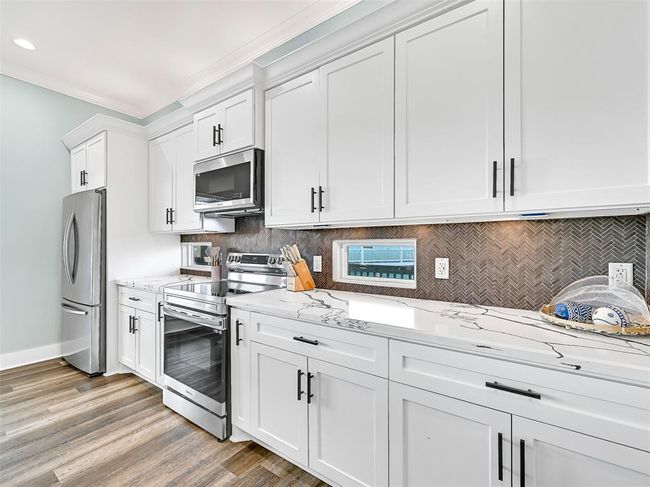 The sleek and functional kitchen features recent stainless steel appliances, soft-close cabinetry, under-cabinet task lighting, and a bold herringbone backsplash punctuated with sunlit clerestory windows for a modern coastal touch. | Image 15