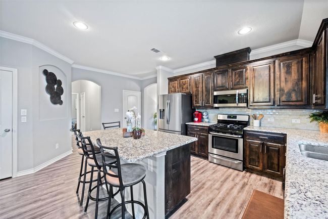 Kitchen featuring stainless steel appliances, arched walkways, a breakfast bar area, light wood-style flooring, and dark brown cabinets | Image 7