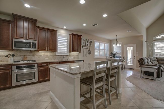 Kitchen with appliances with stainless steel finishes, light tile patterned flooring, light stone countertops, tasteful backsplash, and a chandelier | Image 5