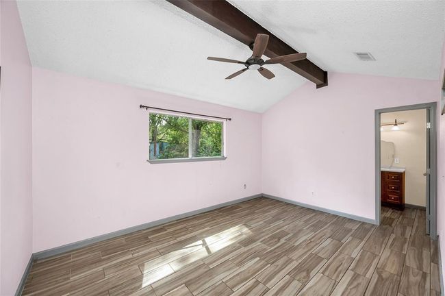 Spacious primary bedroom featuring a vaulted ceiling with exposed beams, large window for natural light, and sleek wood-look tile flooring. | Image 22