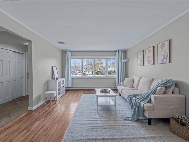 Living room featuring crown molding, wood finished floors, baseboards, visible vents, and a baseboard heating unit | Image 5