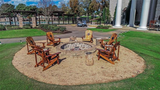Relax and unwind in this beautifully designed outdoor gathering space, featuring a custom stone fire pit surrounded by rustic wooden chairs. Nestled within the Sugar Creek community, this inviting amenity offers a perfect setting for evening conversations and social gatherings. Just steps away, enjoy the lush landscaping, pergola-covered seating areas, and a sparkling pool. Experience the charm and tranquility of Sugar Creek living! | Image 43