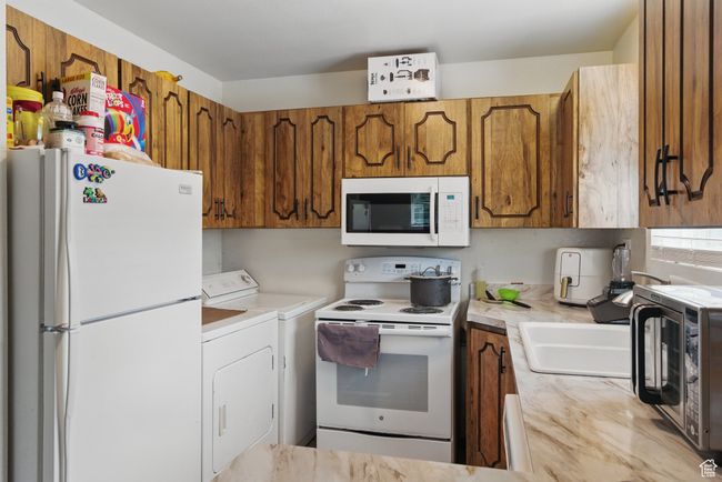 Kitchen with a toaster, separate washer and dryer, white appliances, brown cabinetry, and light countertops | Image 19