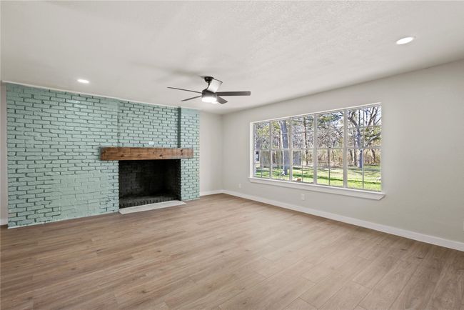 Unfurnished living room with baseboards, a fireplace, a textured ceiling, and light wood finished floors | Image 8