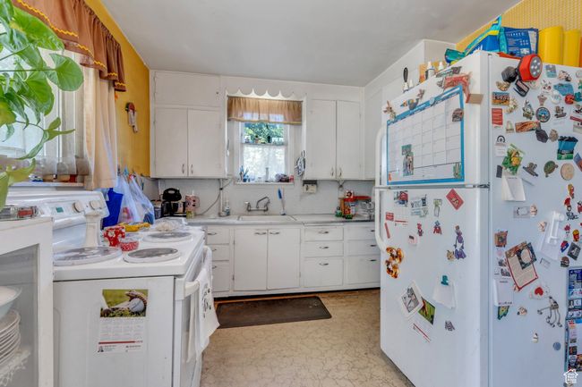 Kitchen featuring freestanding refrigerator, stove, a sink, light countertops, and white cabinetry | Image 5