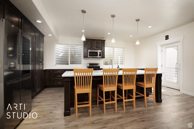 Kitchen featuring light hardwood / wood-style flooring, appliances with stainless steel finishes, hanging light fixtures, a center island, and a kitchen bar | Image 31
