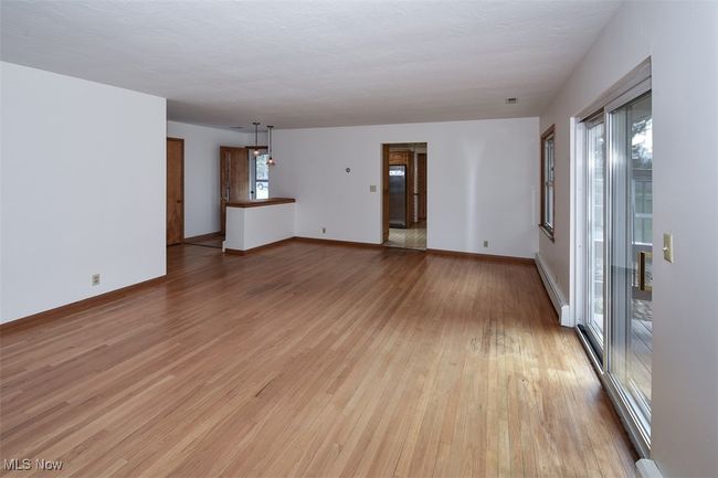 Unfurnished living room with a baseboard heating unit, baseboards, and light wood-style floors | Image 17