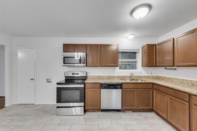 Kitchen featuring brown cabinets, light stone countertops, appliances with stainless steel finishes, and a sink | Image 7