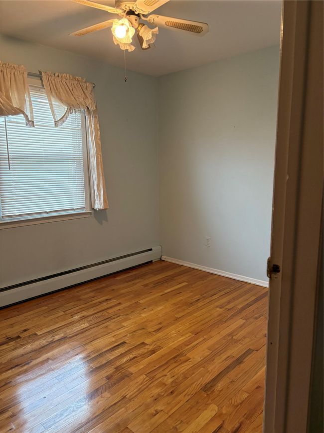 Empty room featuring a baseboard radiator, a ceiling fan, baseboards, and wood finished floors | Image 7