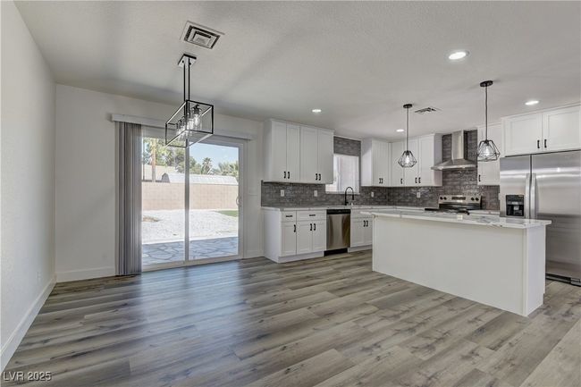Kitchen featuring stainless steel appliances, wall chimney range hood, backsplash, light wood finished floors, and white cabinets | Image 15