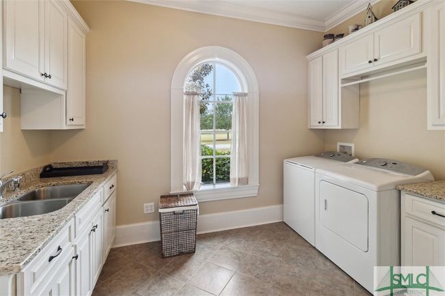 On the other end of the house, next to the kitchen is a well designed laundry area with lots of cabinets, a sink, and a folding table. Not shown is a pull down ironing board. | Image 19