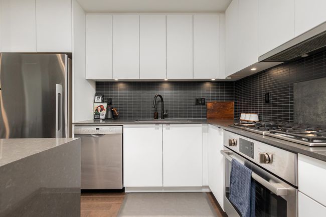 Kitchen with appliances with stainless steel finishes, modern cabinets, dark countertops, tasteful backsplash, and white cabinets | Image 15