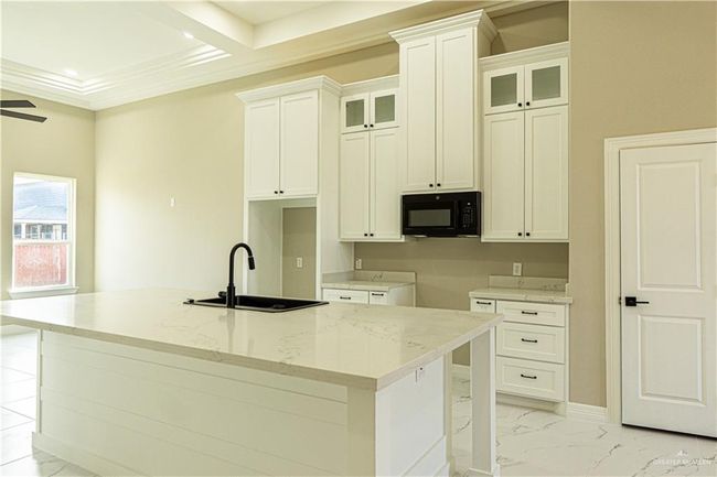 Kitchen with black microwave, a sink, marble finish floor, and an island with sink | Image 13
