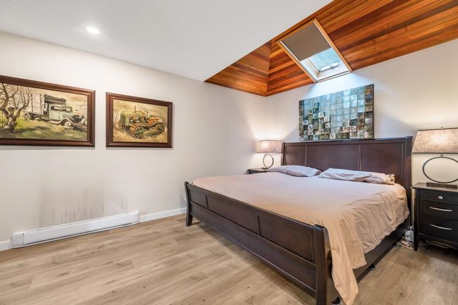 Bedroom featuring a baseboard heating unit, vaulted ceiling with skylight, baseboards, and wood finished floors | Image 12