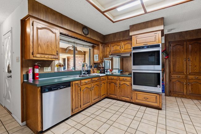 Kitchen with brown cabinetry, under cabinet range hood, a textured ceiling, and appliances with stainless steel finishes | Image 22