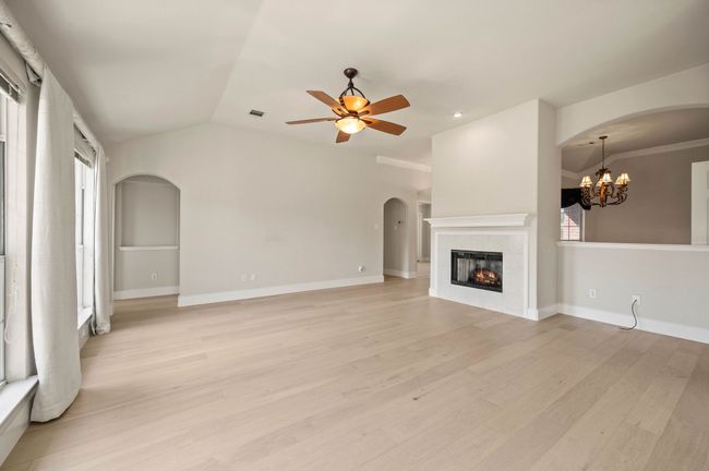 Unfurnished living room with arched walkways, ceiling fan with notable chandelier, light wood-style floors, and vaulted ceiling | Image 11