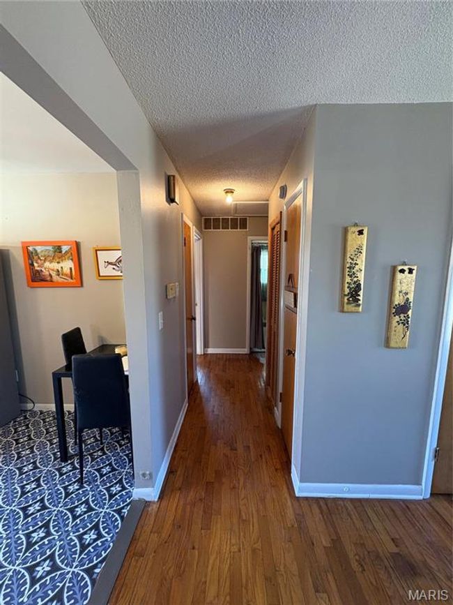 Hallway featuring visible vents, a textured ceiling, baseboards, and hardwood / wood-style flooring | Image 13