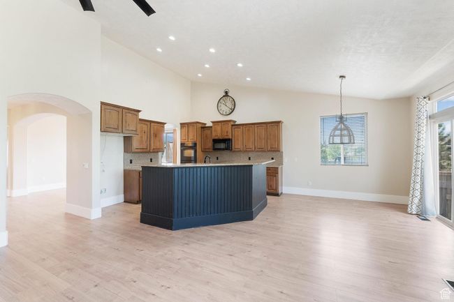 Kitchen with black appliances, brown cabinetry, a center island with sink, arched walkways, and light wood-style flooring | Image 12