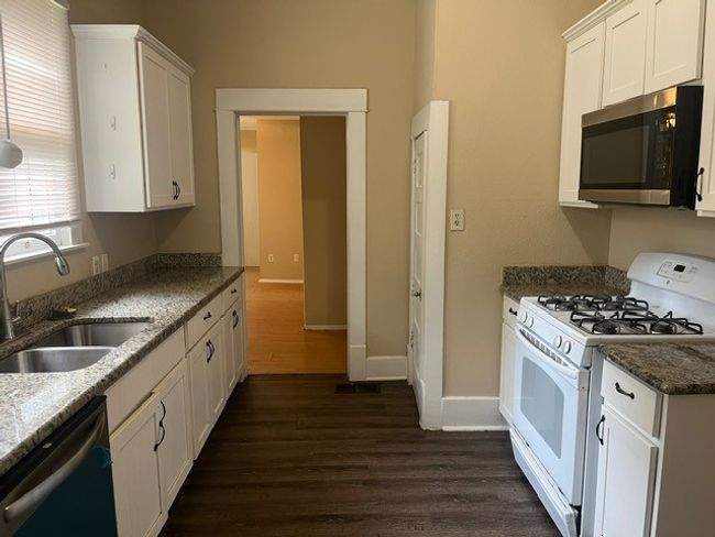 Kitchen with appliances with stainless steel finishes, dark wood finished floors, white cabinetry, and dark stone counters | Image 9