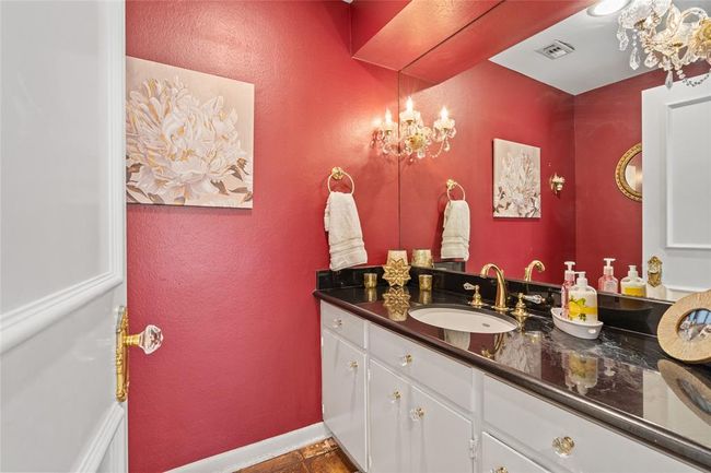 This elegant half bath makes a bold statement with rich red walls, a sleek black granite countertop, and gold fixtures adding a touch of sophistication. The oversized mirror enhances the space, while crystal-accented lighting provides a warm, inviting glow. Perfect for guests to use, this stylish powder room offers both charm and functionality! | Image 32