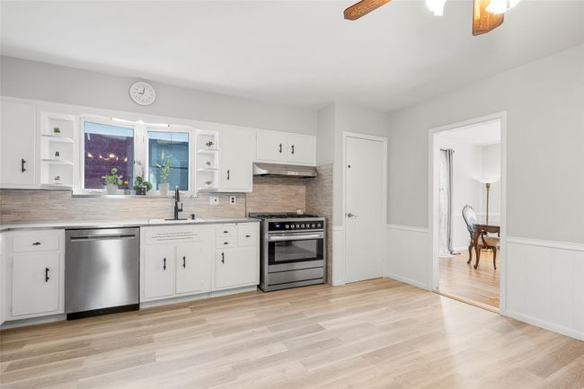 Kitchen featuring appliances with stainless steel finishes, exhaust hood, open shelves, a sink, and wainscoting | Image 9