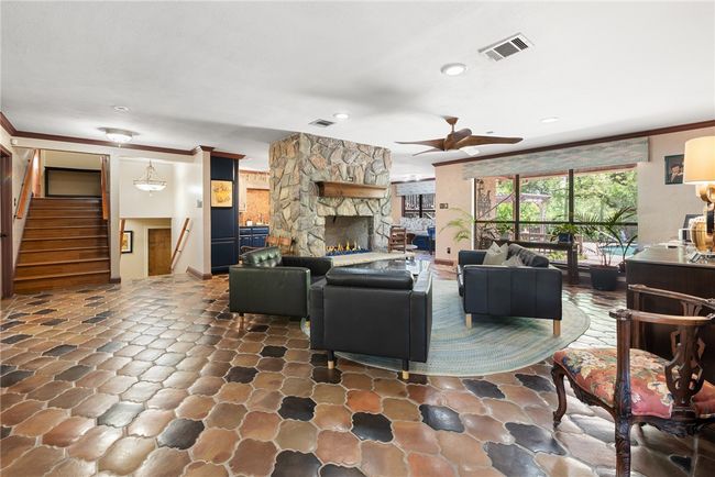 Living area featuring a stone fireplace, ornamental molding, stairs, visible vents, and ceiling fan | Image 16