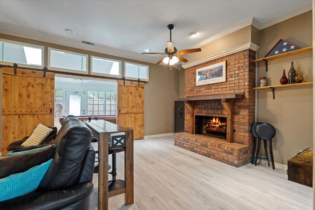 Living area with light wood finished floors, a brick fireplace, ceiling fan, crown molding, and baseboards | Image 9