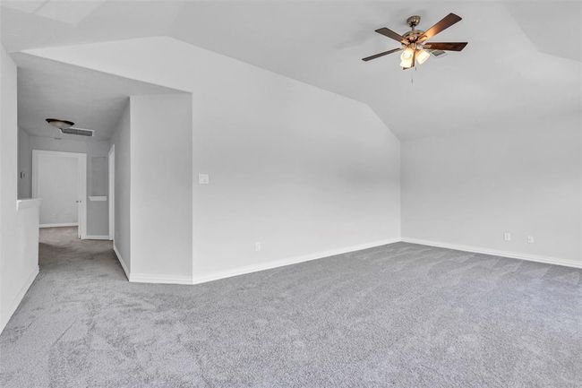 This spacious room features soft gray carpeting, a ceiling fan, and ample natural light. The neutral walls provide a blank canvas for personalization, and the adjacent hallway leads to additional rooms, offering flexibility for various uses. | Image 41