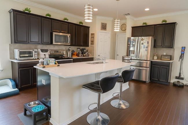 Kitchen featuring appliances with stainless steel finishes, backsplash, dark brown cabinetry, a breakfast bar area, and crown molding | Image 4
