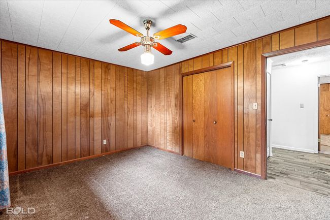 Unfurnished bedroom with carpet flooring, wooden walls, a closet, and ceiling fan | Image 21