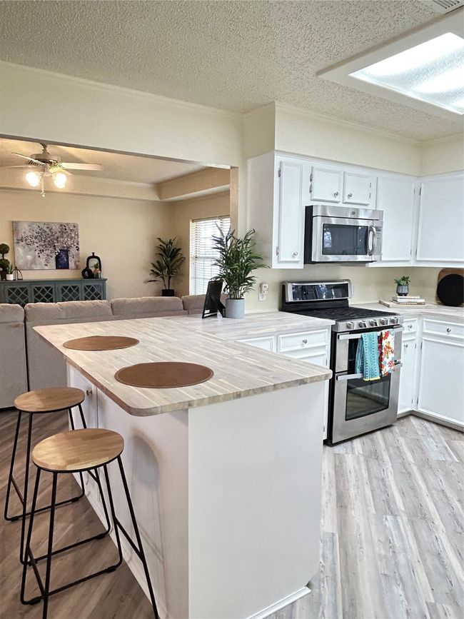 Kitchen with light wood finished floors, light countertops, white cabinets, a kitchen bar, and range | Image 13