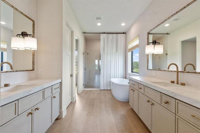 Expertly appointed, the walls are clad in a neutral, yet textural large format tile. The large pane mirrors feature a decorative trim to repeat the warm wood tones in the space. Kohler premium plumbing hardware punctuate the elegance. Not shown is the water closet with Kohler's top-of-the-line toilet and bidet/washlet fixture. Cosentino porcelain countertop materials are repeated as details in the shower for continuity. | Image 19