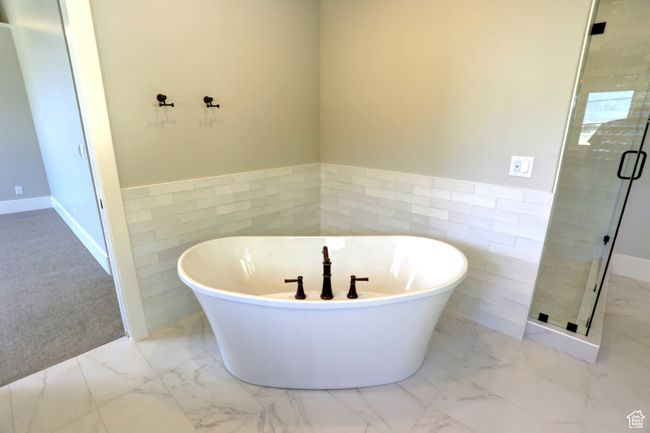 Bathroom featuring tile walls, marble finish flooring, a stall shower, a soaking tub, and a wainscoted wall | Image 28