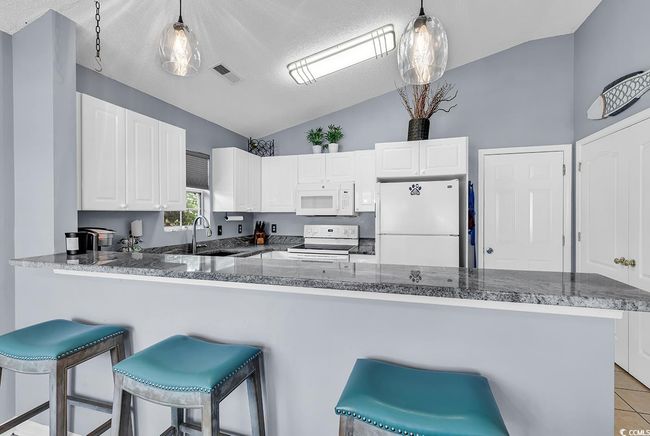 Kitchen with white appliances, vaulted ceiling, white cabinetry, decorative light fixtures, and a breakfast bar | Image 22