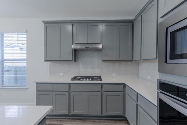 Kitchen with stainless steel appliances, under cabinet range hood, light countertops, decorative backsplash, and gray cabinetry | Image 14