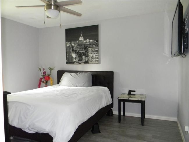 This bedroom features a modern design with light gray walls and wood flooring. | Image 12