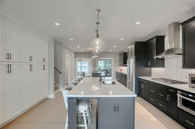 This stylish dining area features a bold modern light fixture, sleek glass table, and built-in buffet cabinetry—flowing effortlessly to a covered balcony and bright flex space framed by French doors. Also features a prep sink! | Image 11