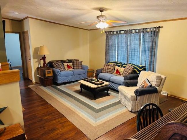 Living room with ceiling fan, a textured ceiling, crown molding, and dark wood finished floors | Image 5