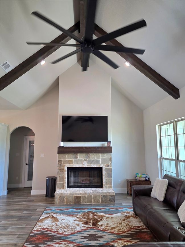 Living room featuring beam ceiling, a stone fireplace, wood finished floors, arched walkways, and recessed lighting | Image 5