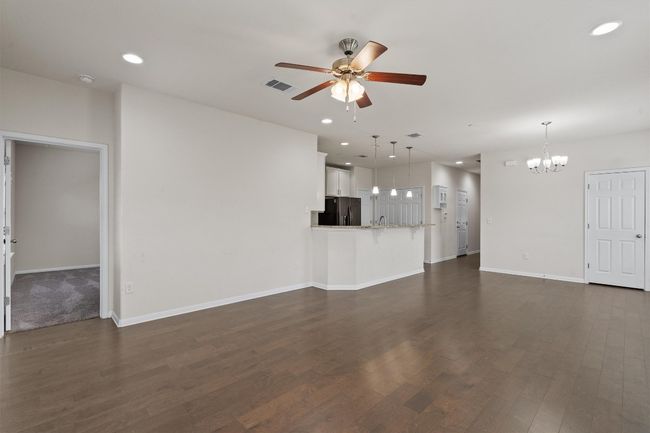 Unfurnished living room with ceiling fan, a chandelier, dark wood-type flooring, baseboards, and recessed lighting | Image 9