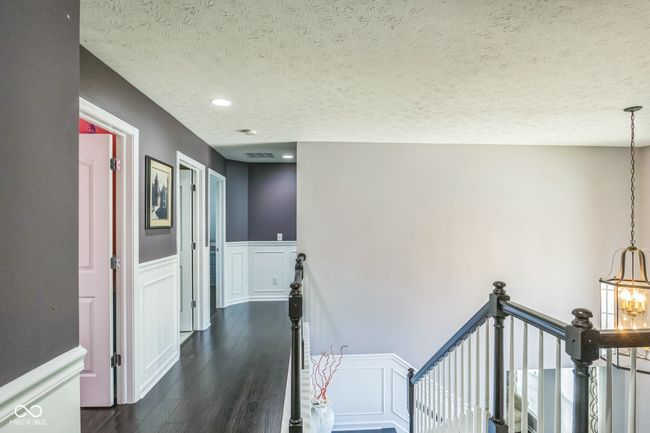 hallway with dark wood-type flooring, a textured ceiling, wainscoting, an upstairs landing, and a chandelier | Image 18