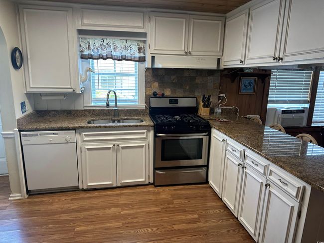 Kitchen featuring dishwasher, stainless steel gas stove, ventilation hood, and wood finished floors | Image 7