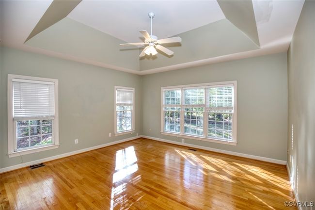 Unfurnished room with wood finished floors, ceiling fan, a raised ceiling, baseboards, and visible vents | Image 21