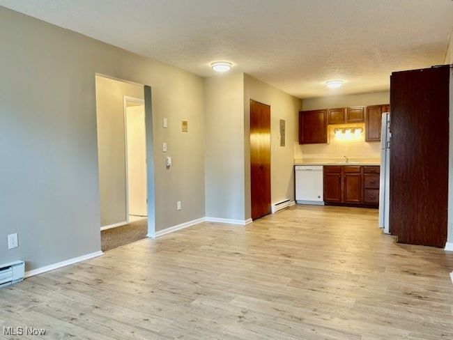 Kitchen with white appliances, light countertops, light wood-type flooring, and a baseboard radiator | Image 5