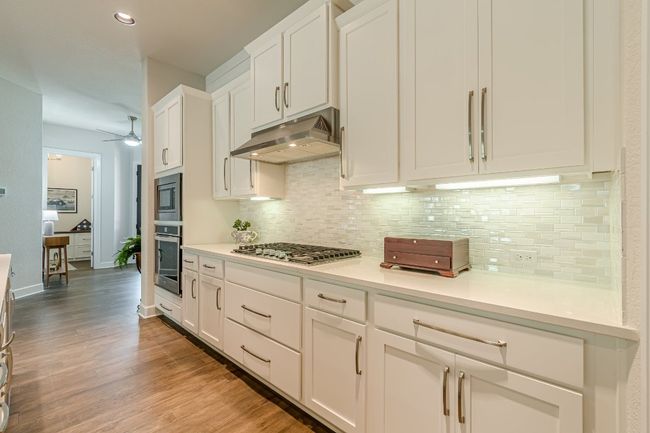Kitchen featuring stainless steel appliances, under cabinet range hood, backsplash, light wood-type flooring, and white cabinets | Image 13