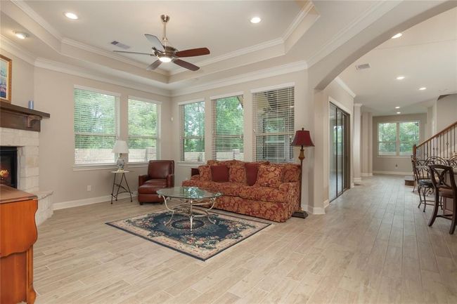 This spacious living area features a cozy fireplace, large windows providing natural light, and elegant tile flooring. The open layout flows into the kitchen and dining space, perfect for entertaining. | Image 10