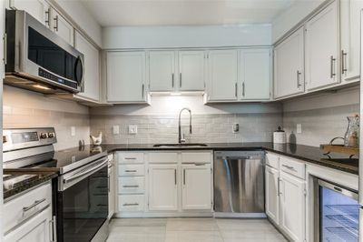 Kitchen featuring stainless steel appliances, white cabinetry, beverage cooler, and sink | Image 3